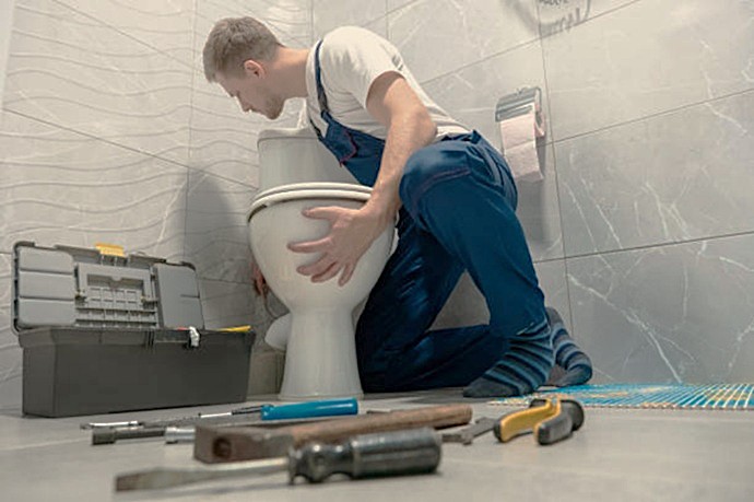 Técnico fontanero cualificado de Multiservice A.D. revisando el mecanismo interno y el sellado de la base de un inodoro para localizar fugas de gases con malos olores o pérdidas de agua.