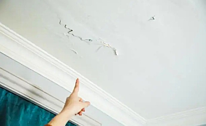 Residente señalando la propagación de una mancha de filtración hídrica y desprendimiento de pintura en el falso techo de un apartamento.