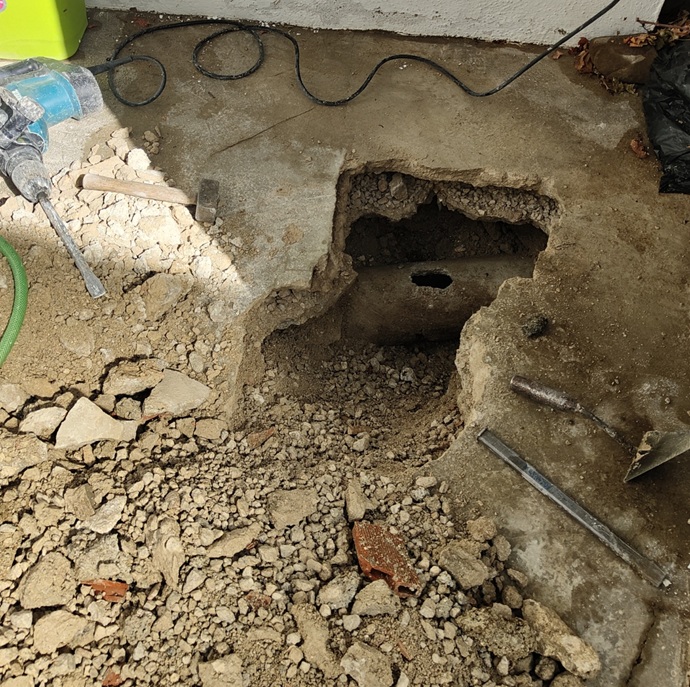 Punto de inspección y apertura manual para localizar la rotura estructural de un colector de saneamiento antiguo mediante martillo demoledor.