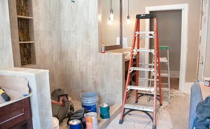 Perspectiva de una zona húmeda en pleno proceso de transición con escaleras de trabajo, materiales de revestimiento y herramientas de preparación para el paramento.