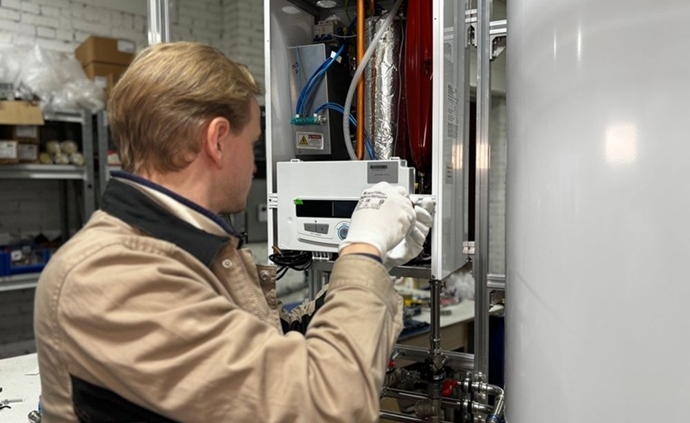 Técnico de Multiservice A.D. con guantes de protección realizando el ajuste de los circuitos electrónicos de un calentador para verificar su correcto arranque térmico.