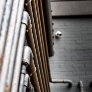 Perspectiva cenital de múltiples líneas de conducción metálica dispuestas en paralelo sobre un muro exterior, evidenciando un alto grado de oxidación y degradación por salinidad acumulada. Multiservice A.D. analiza múltiples líneas de conducción metálica dispuestas en paralelo sobre un muro exterior, evidenciando un alto grado de oxidación y degradación por salinidad acumulada.