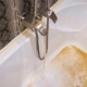 Caudal de agua con alta saturación ferrosa de tonalidad ámbar emanando de una grifería y manchando el fondo de una bañera doméstica.