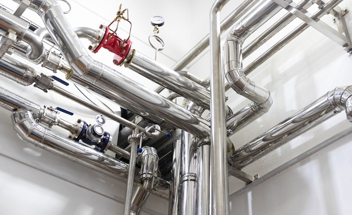 Complejo entramado de fontanería industrial con tuberías de acero inoxidable, manómetros de presión y válvulas de cierre en una sala técnica impecable.