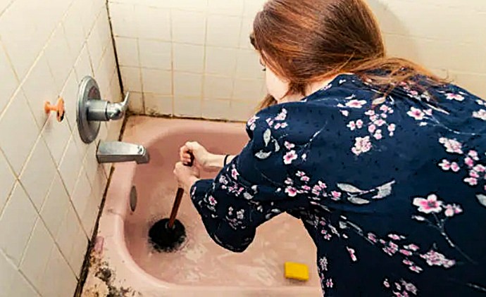 Técnica de desatoro manual mediante presión negativa con ventosa profesional para movilizar tapones orgánicos en el fondo de una bañera.